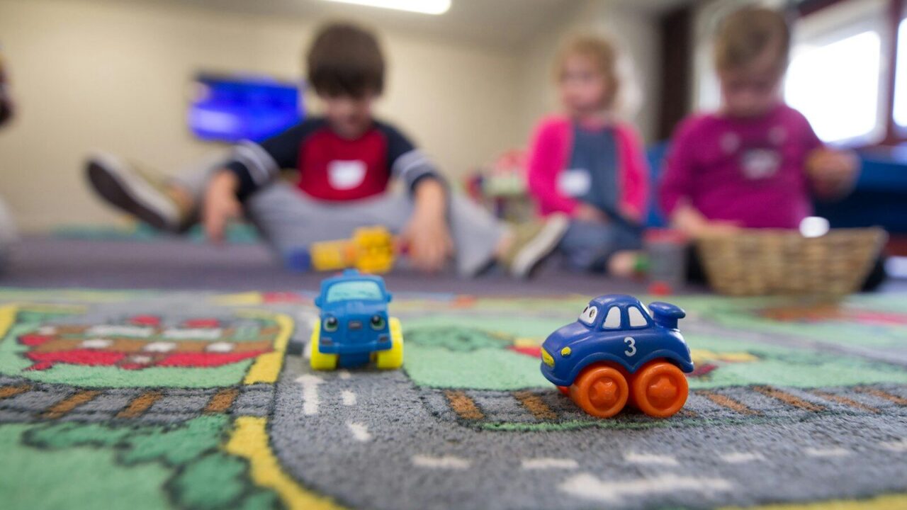 Een groep jonge kinderen speelt samen met speelgoed op de vloer in een kleurrijke opvang- of speelruimte.