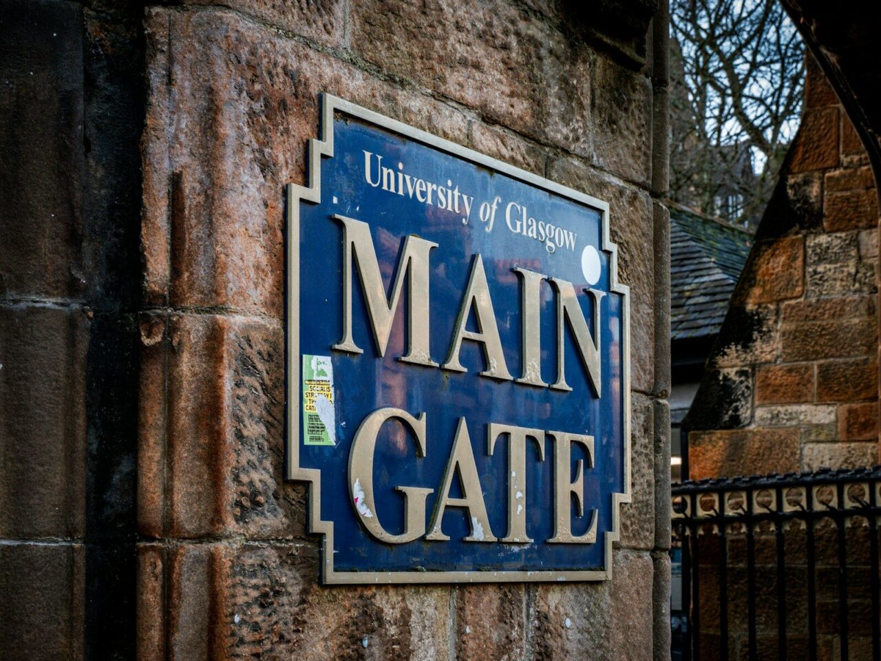 a blue sign that reads main gate on a brick wall