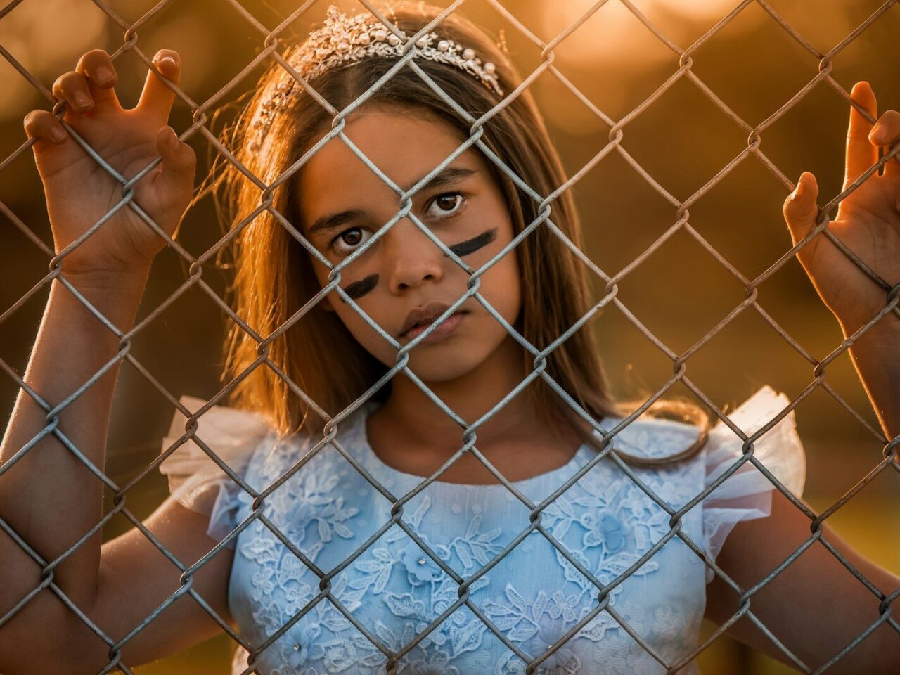 Young girl in tiara behind chain-link fence